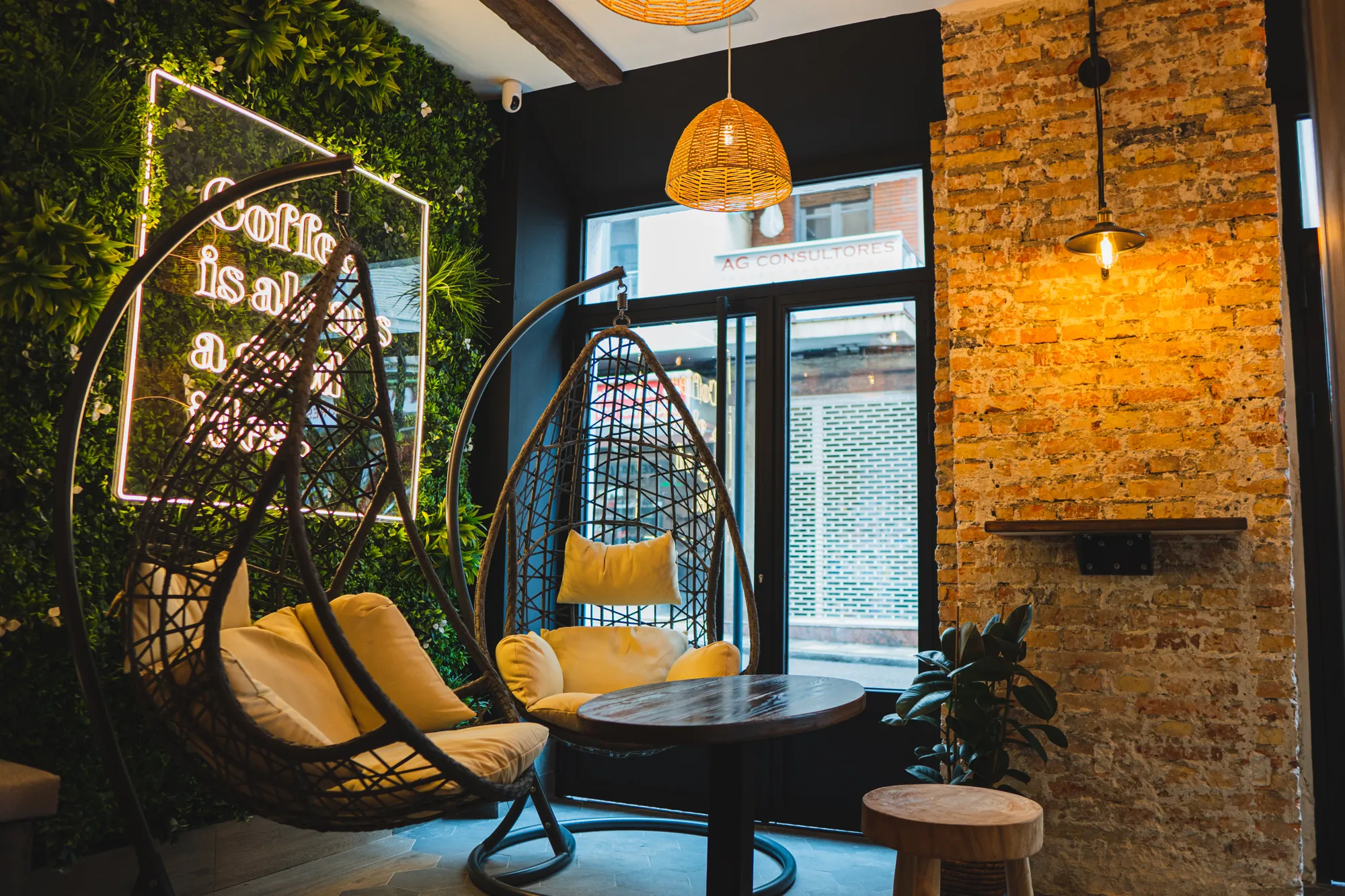 Interior de Melatte con sillas colgantes, pared vegetal y ladrillo visto